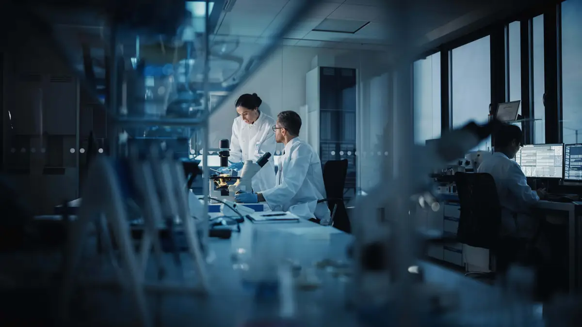 Two scientists in lab coats reviewing data on a computer screen in a laboratory setting, with the Waters Xevo TQ-XS System in the background, used for exhaled breath testing.
