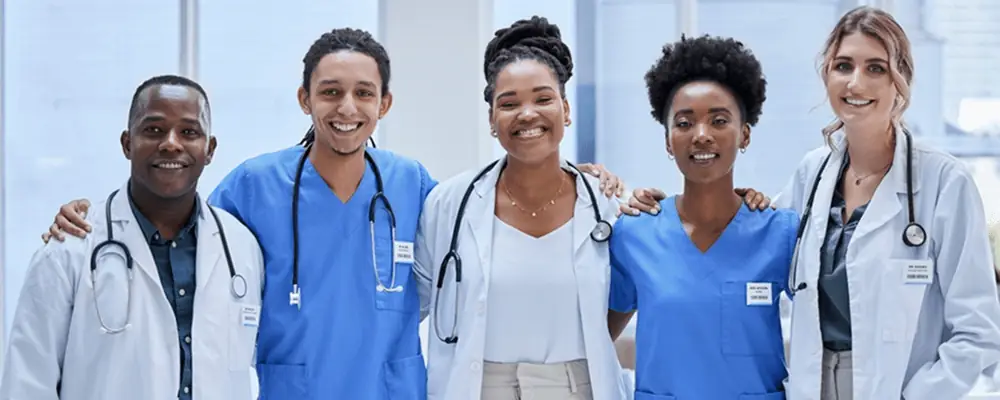 Diverse group of smiling healthcare professionals, including doctors and nurses, standing together in a modern medical facility.