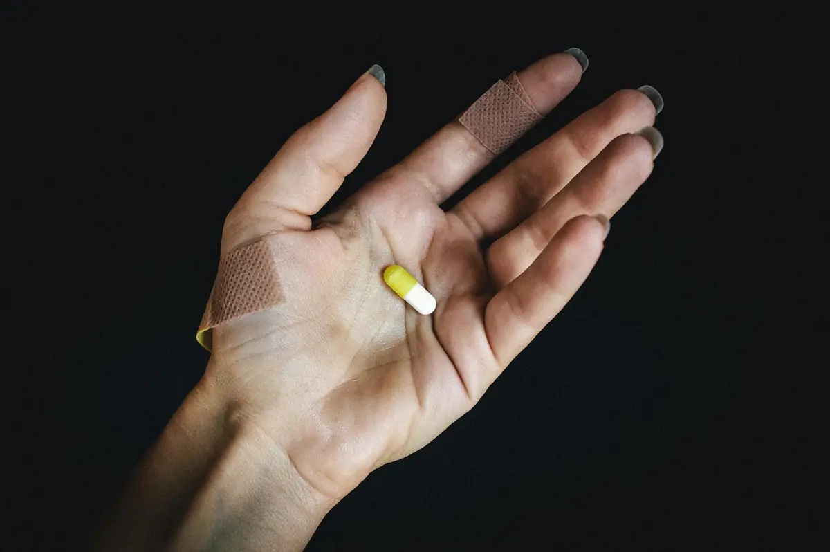 Close-up of a hand with bandages holding a single pill, representing substance use and prevention