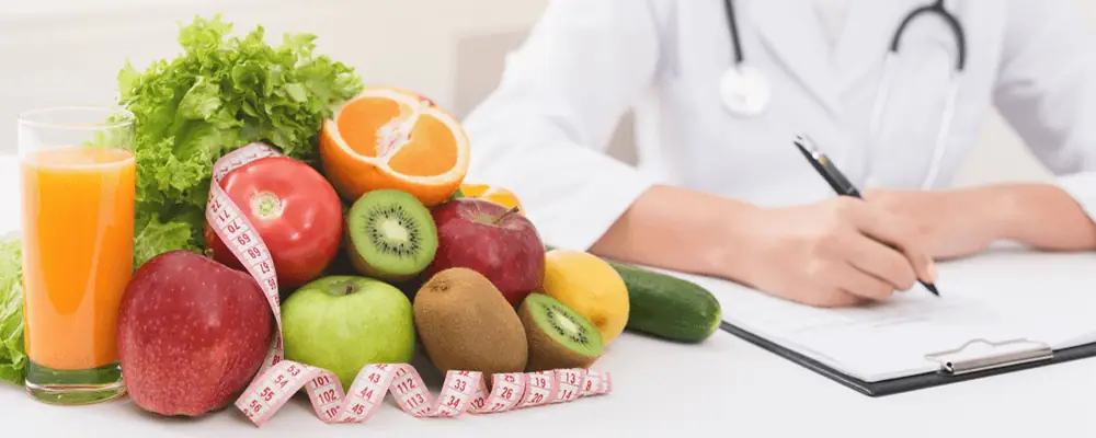 Fresh fruits and vegetables with juice, tape measure, and nutritionist writing diet plan – concept of healthy eating and weight loss resolution