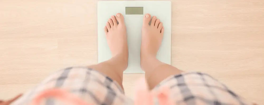 Person checking body weight on digital scale as part of a weight loss plan to lower high blood pressure and improve heart health.