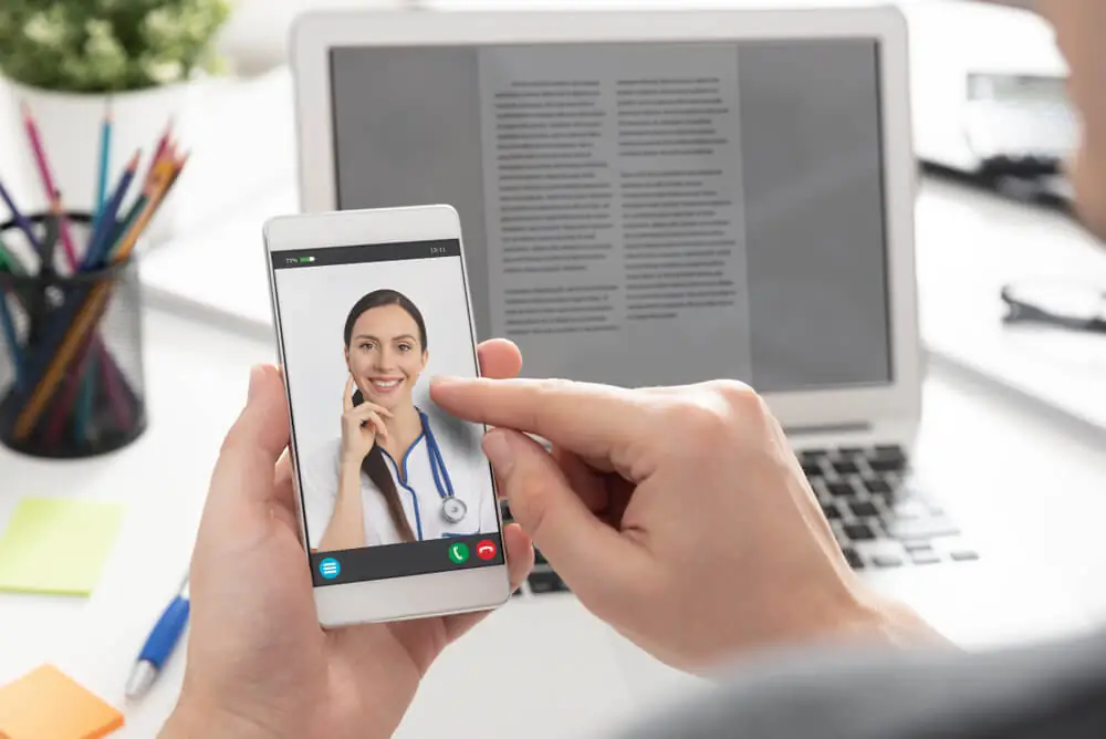 Patient having a virtual telehealth appointment with a female doctor via smartphone, highlighting integrated primary care, psychiatry, and addiction treatment access through Omega Physicians' remote healthcare services.
