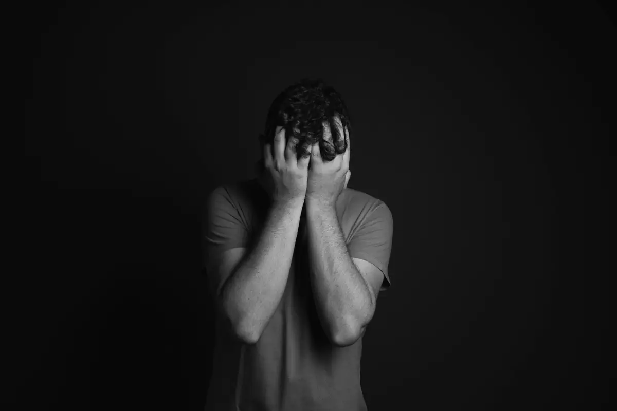 Black and white image of a man holding his face in reflection, symbolizing the importance of compassion and understanding during Mental Illness Awareness Week.